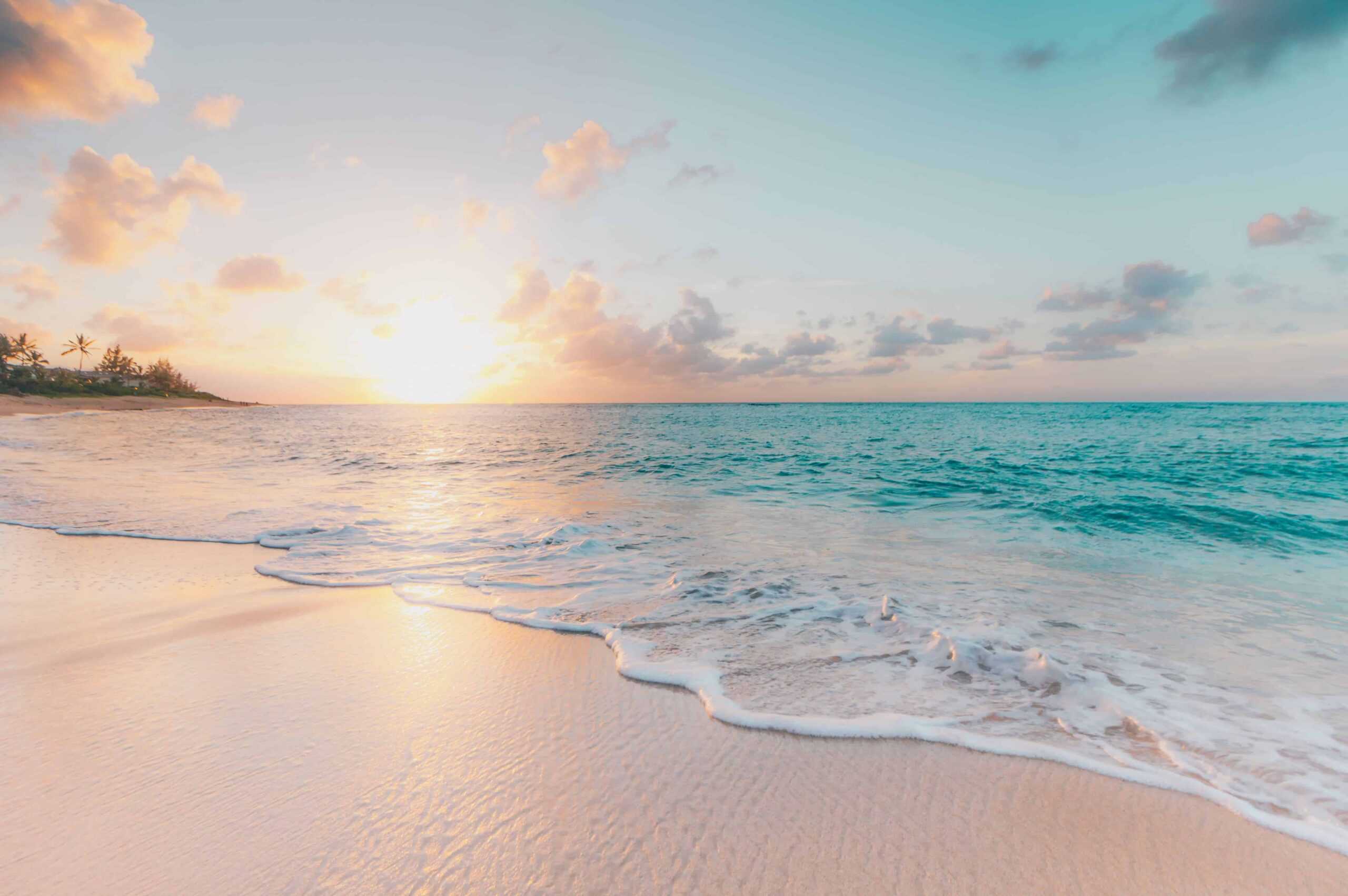 A warm sunrise over a beach with a small wave over the golden sand