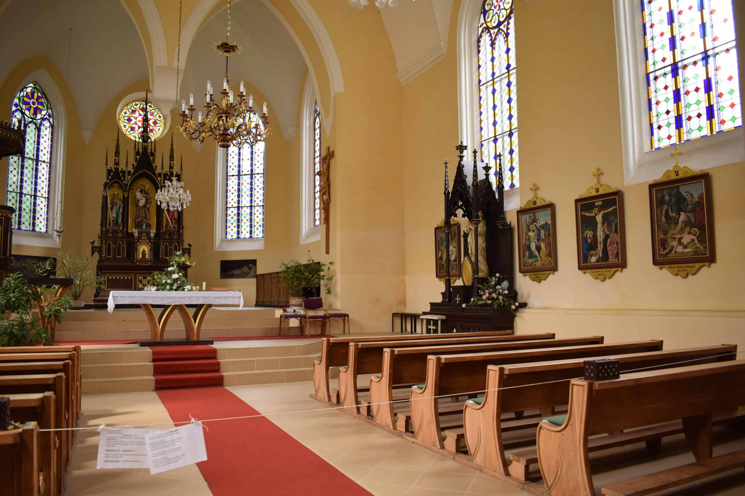 inside a religious building, looking at the wooden pews, paintings, and stained glass windows. The later is seen at the end.