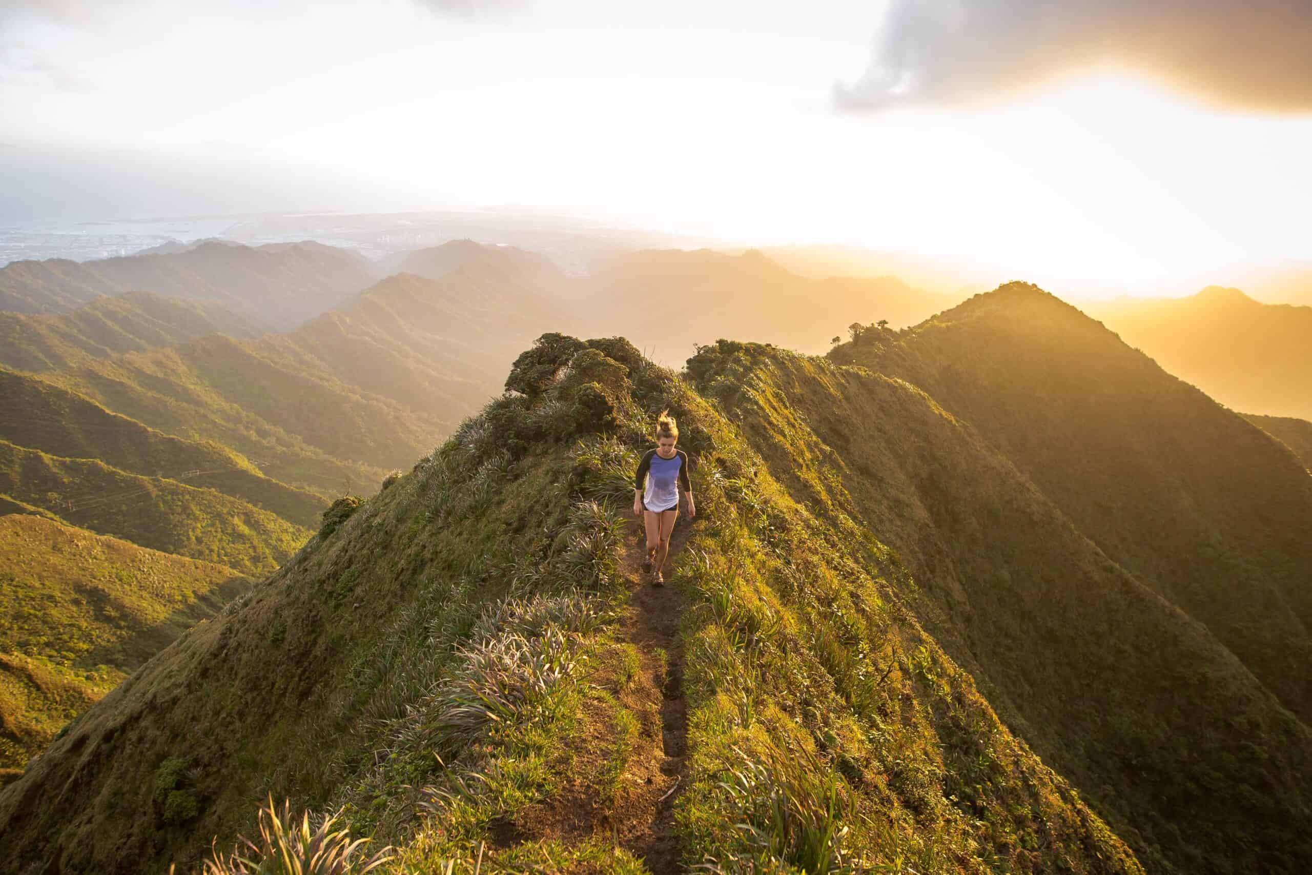 a woman running on a path on the top of a green, grassy mountain, with golden light