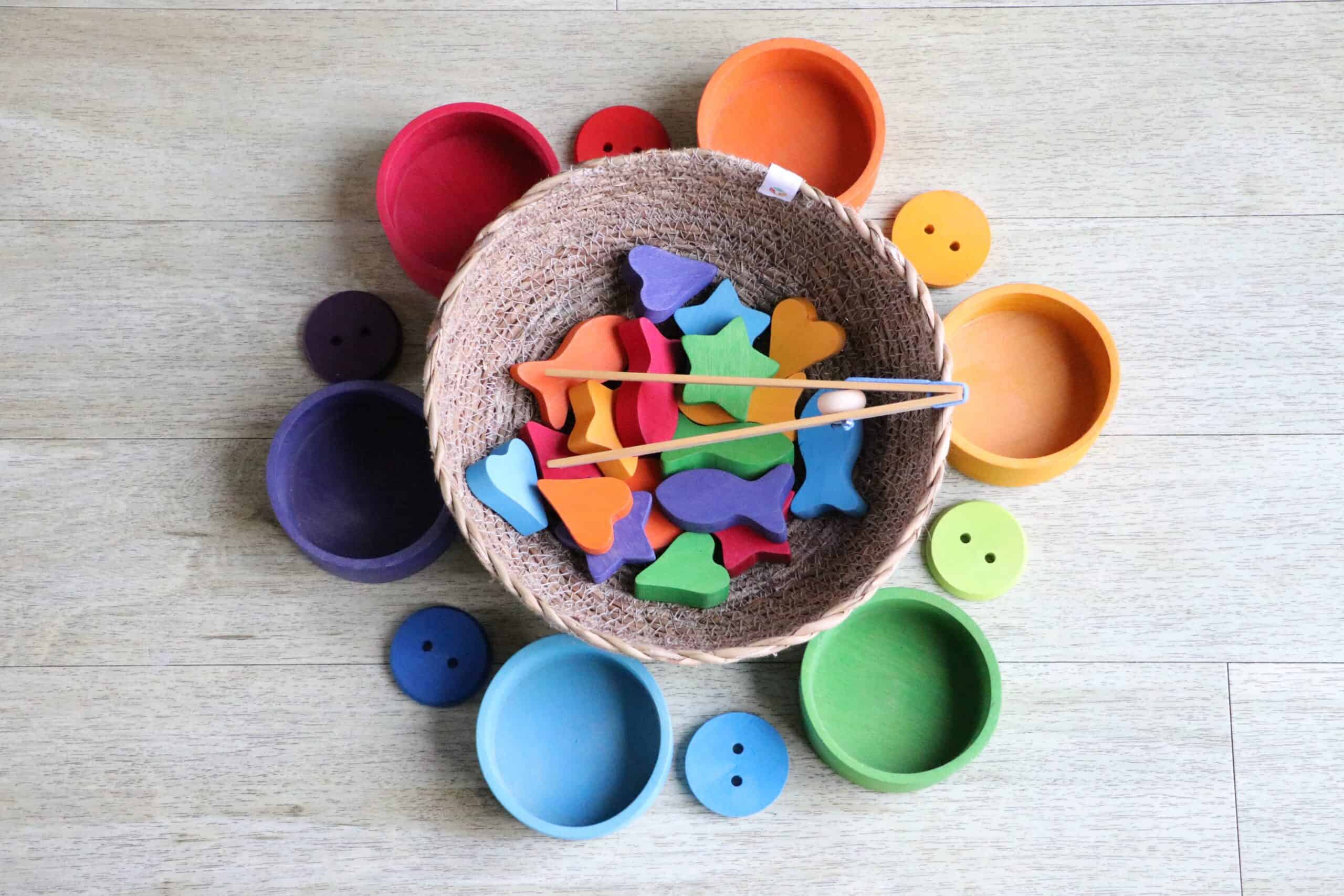 a bowl of wooden fish, stars and hearts, with smaller brightly coloured bowls around it, and chopsticks. It might be a game to sort the coloured items into the bowls,