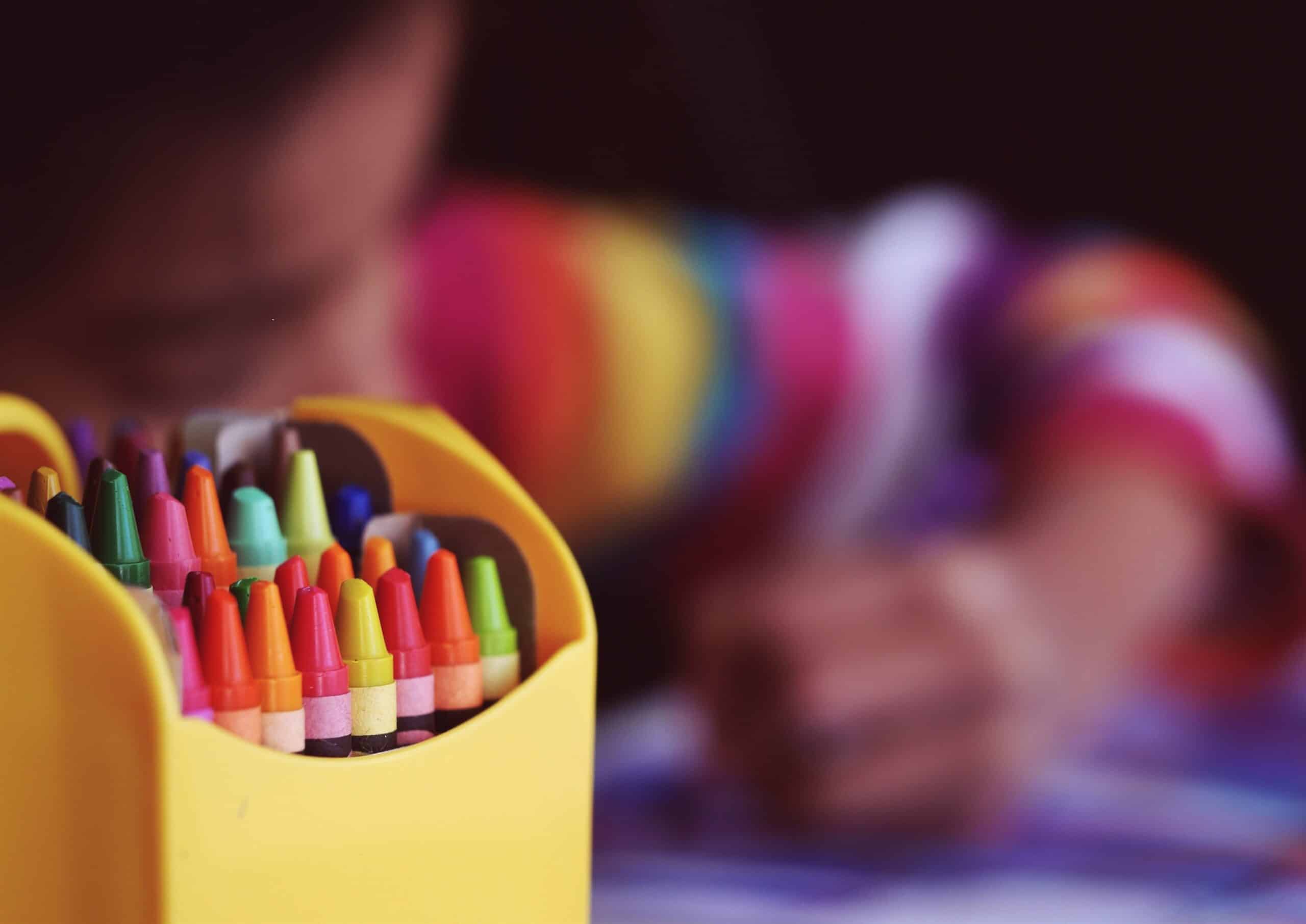 close up of colourful crayons and a child using them to draw